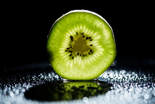 slice of fresh kiwi fruit on black background with bokeh - Foto, imagen