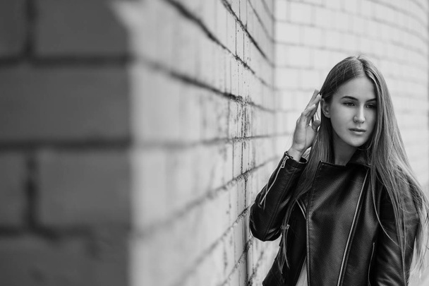 Young beautiful caucasian girl posing in a black leather jacket on a brick wall background. - 写真・画像