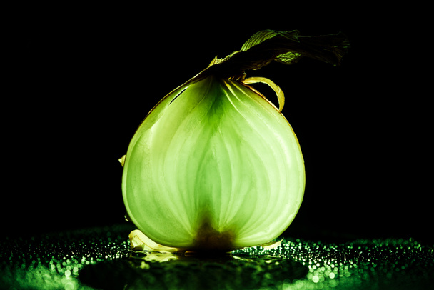 slice of raw onion with water drops and neon green back light on black background - Photo, Image