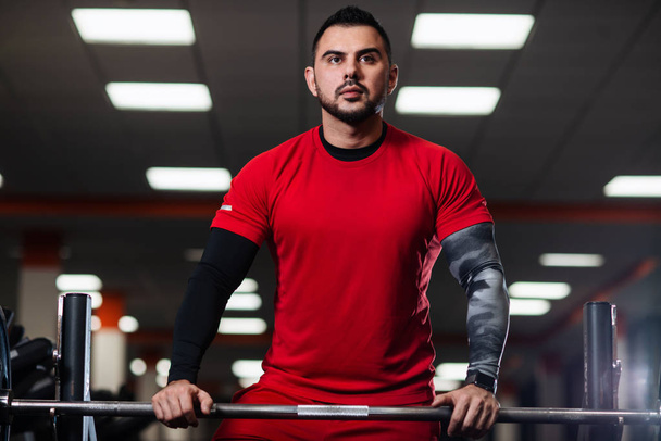 Handsome man with big muscles, posing at the camera in the gym in red clothes - Foto, Imagem