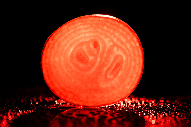 slice of raw onion with water drops and neon red back light on black background - Zdjęcie, obraz