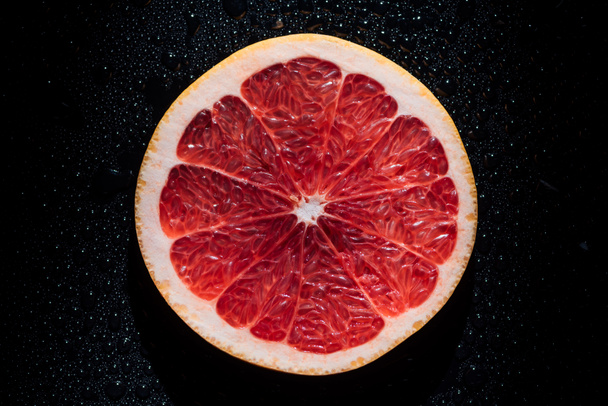 Scheibe Grapefruit auf schwarzem Hintergrund mit Wassertropfen - Foto, Bild