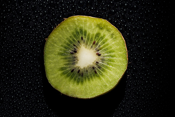 slice of fresh kiwi fruit on black background with water drops - Photo, Image