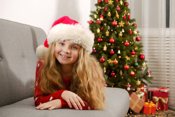 Portrait of cute happy nine year old girl wearing red christmas sweater with many presents, Decorated Christmas tree with stack of wrapped gifts on background. Close up, copy space. - Photo, Image