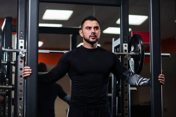 Handsome with big muscles in black clothes posing next to the barbell - Foto, immagini