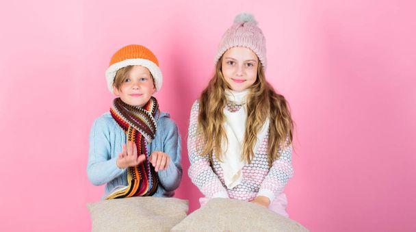 Stay warm and comfortable. Warm up your winter wear with cute and cozy accessories. Siblings wear winter warm hats sit on pink background. Children boy and girl warm up with pillows and hats - Foto, afbeelding