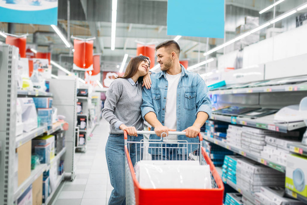 Couple with cart in a supermarket, family shopping. Customers in shop, buyers choosing consumer goods - Foto, Imagen