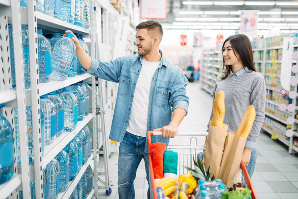 A fiatal pár kosár vesz kanna vizet a polcról egy szupermarketben, családi vásárlás. A(z) bolt, vevők piacon, gyerekeknek áruk Tanszék - Fotó, kép