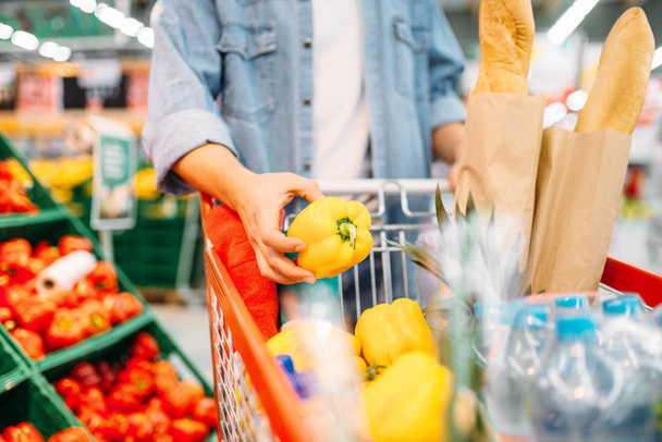 Maschio mette pepe giallo nel carrello con prodotti in un supermercato, shopping di famiglia. Cliente in negozio, acquirente nel mercato
 - Foto, immagini