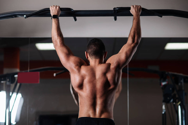 Brutal athletic man making pull-up exercises on a crossbar in the gym - 写真・画像