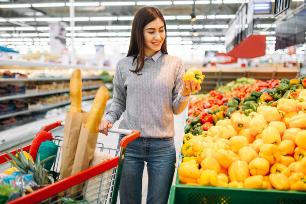 Donna con carrello che sceglie peperoni gialli dolci freschi in un supermercato, shopping di famiglia. Cliente donna in negozio, acquirente nel mercato
 - Foto, immagini