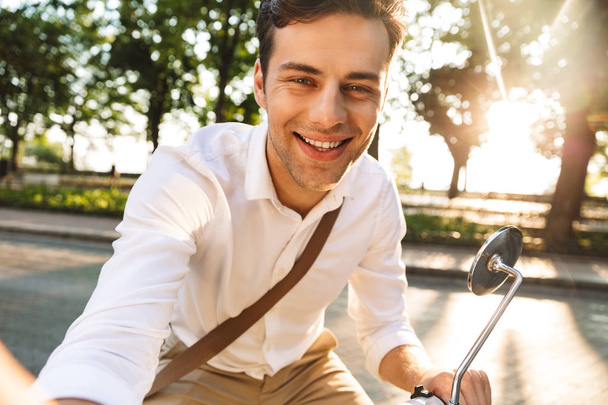 Foto eines hübschen aufgeregten jungen Geschäftsmannes, der auf seinem Roller im Freien spaziert, macht ein Selfie mit der Kamera. - Foto, Bild