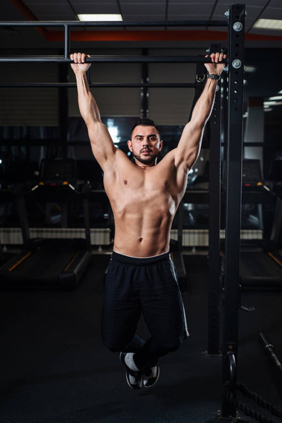 Brutal athletic man making pull-up exercises on a crossbar in the gym - 写真・画像