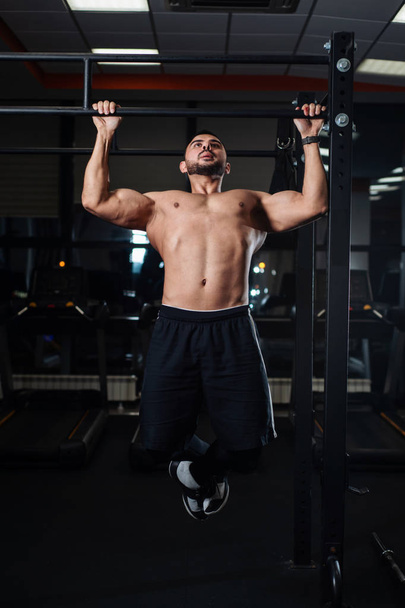 Brutal athletic man making pull-up exercises on a crossbar in the gym - Zdjęcie, obraz