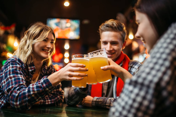 Футбольные болельщики пьют пиво за столом в спортивном баре. Празднование победы, телевизионное вещание, развлечения юных друзей в пабе
 - Фото, изображение