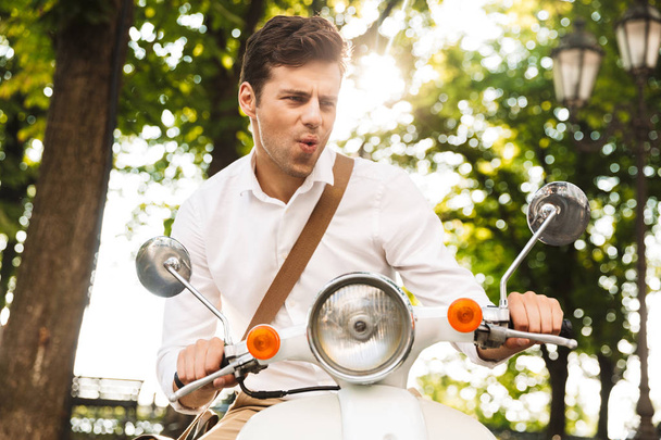 Excited young businessman riding on a motorbike outdoors at the city park - 写真・画像
