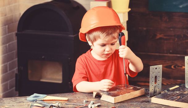 Boy play as builder or repairer, work with tools. Kid boy in orange hard hat or helmet, study room background. Child dreaming about future career in architecture or building. Childhood concept - 写真・画像