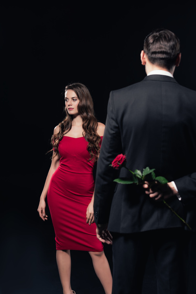 man hiding rose behind back with woman in red dress on background isolated on black - 写真・画像