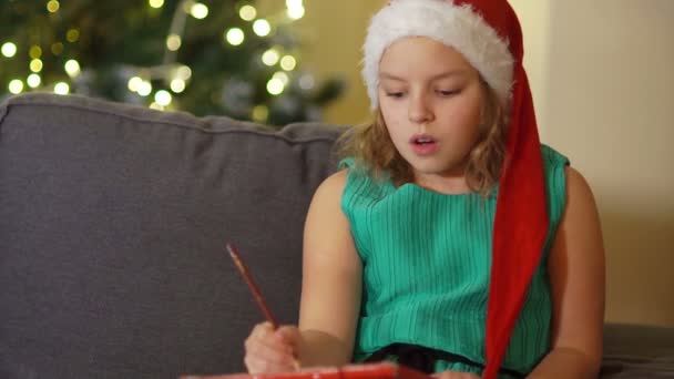 Teen girl writes a letter to Santa Claus. Preparing for Christmas, makes wishes, New Years traditions - Кадри, відео
