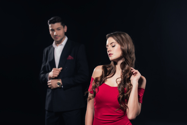 selective focus of beautiful woman in red dress with man on background isolated on black - Photo, Image