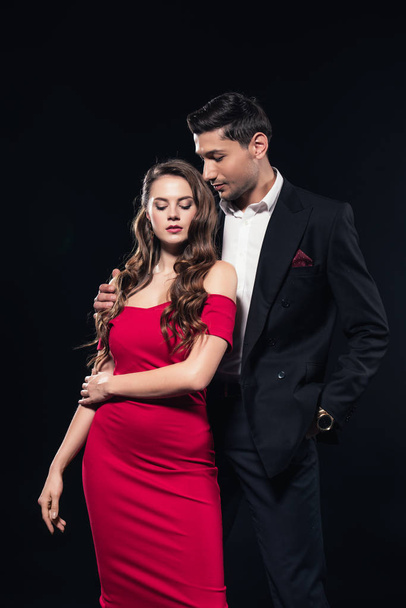 handsome man embracing beautiful woman in red dress isolated on black - Fotografie, Obrázek