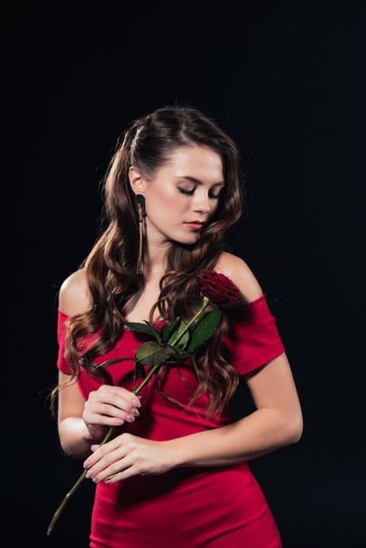 woman with eyes closed in red dress holding rose isolated on black - Foto, Bild