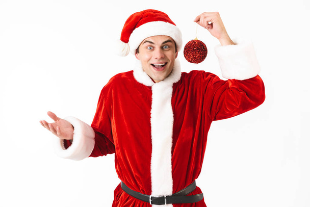 Image of european man 30s in santa claus costume and red hat holding new year red ball isolated on white background in studio - Foto, Imagen