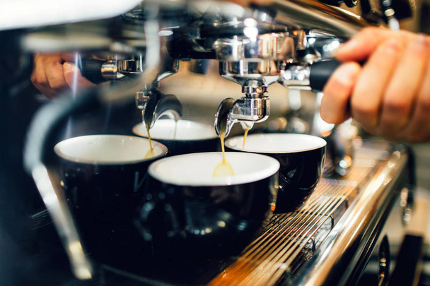 Close up and cut view of mans hand holding cezve from coffee machine above two cups. Coffee is pouring out from it into cups. - Фото, зображення