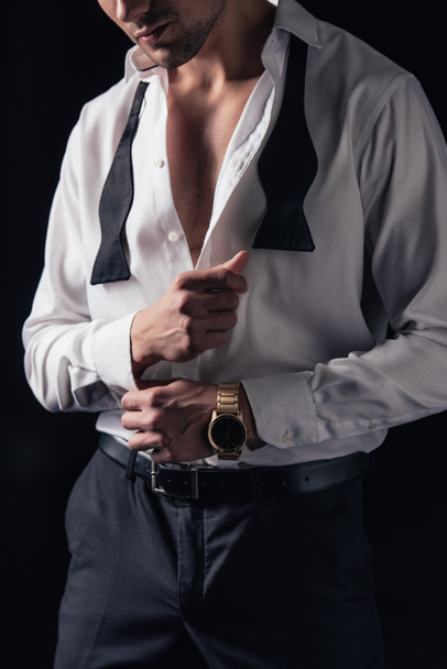 περικοπεί θεώρηση του ανθρώπου κουμπιά από λευκό πουκάμισο που απομονώνονται σε μαύρο - Φωτογραφία, εικόνα