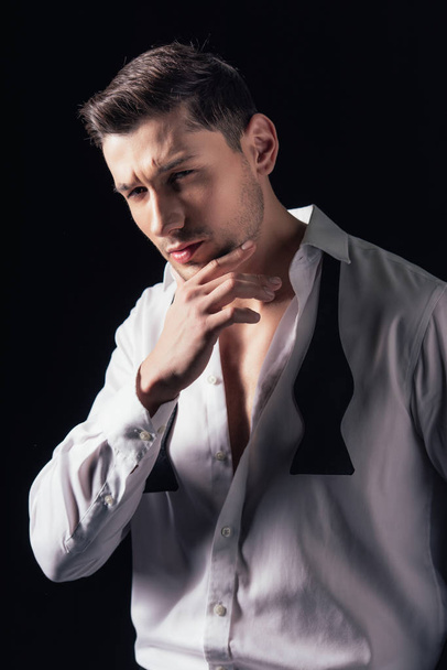 man in white shirt looking at camera, touching chin and posing isolated on black - Foto, Imagem