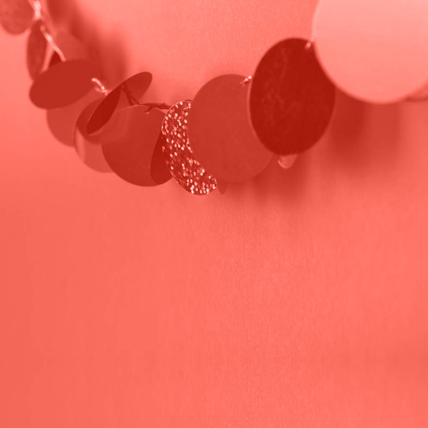 Girlanden hängen aus glänzenden Kreisen auf Korallengrund. Festliche Dekoration. Kopierraum für Text. Farbe des Jahres 2019. lebende Koralle. - Foto, Bild
