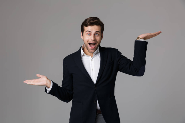 Image of surprised businessman 30s in formal suit screaming and throwing up arms isolated over gray background - Фото, зображення