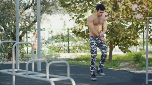 Young athlete jumps with a skipping rope on the sport ground in summer park - Filmagem, Vídeo