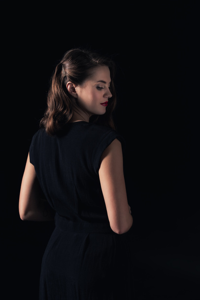 back view of beautiful woman in dress posing isolated on black - 写真・画像