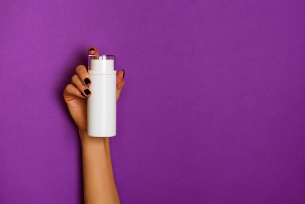 Female hands holding white cosmetic bottle on violet background. Banner. Skin care, pure beauty, body treatment concept - Φωτογραφία, εικόνα