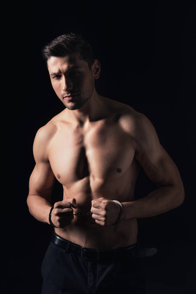 handsome shirtless man in handcuffs looking at camera isolated on black - Foto, Imagem