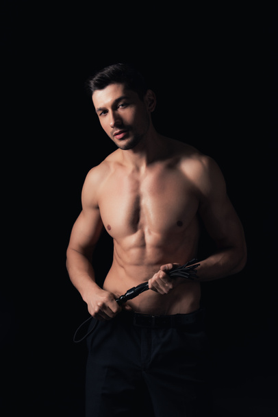shirtless man looking at camera and holding leather flogging whip isolated on black - Foto, Imagem