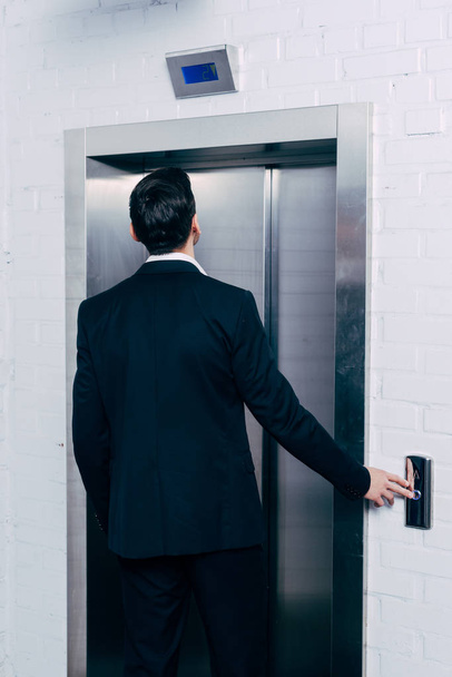 back view of man in black suit pressing elevator button - Zdjęcie, obraz