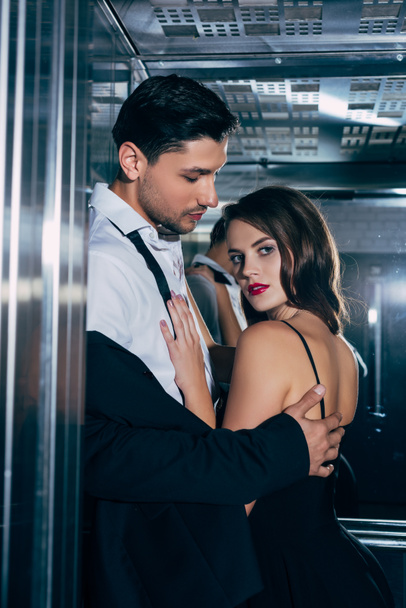 beautiful woman looking at camera man and embracing handsome man in elevator - Φωτογραφία, εικόνα