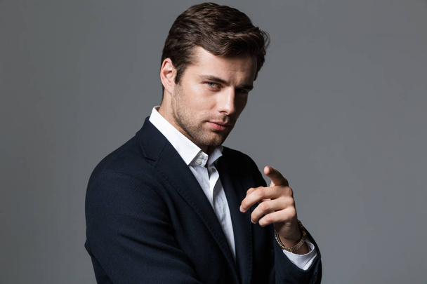 Close up portrait of a handsome young businessman dressed in suit isolated over gray background, pointing finger at camera - Фото, зображення