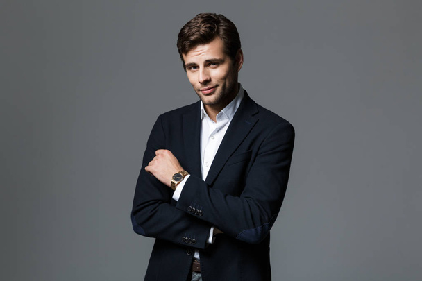 Portrait of a handsome young businessman dressed in suit isolated over gray background, looking at camera - Фото, зображення
