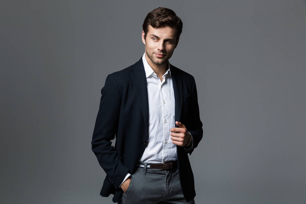 Portrait of a handsome young businessman dressed in suit isolated over gray background, looking away - Photo, Image