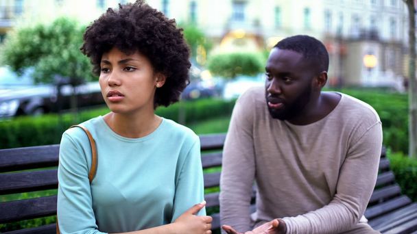 Young man talking to offended girlfriend on bench, jealous woman, break up - Zdjęcie, obraz