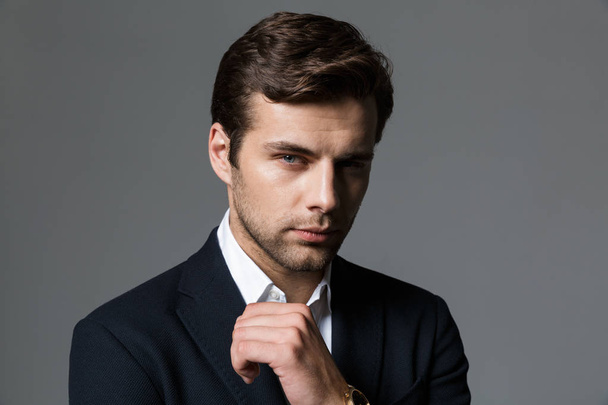 Close up portrait of a confident young businessman dressed in suit isolated over gray background, looking at camera - Фото, зображення