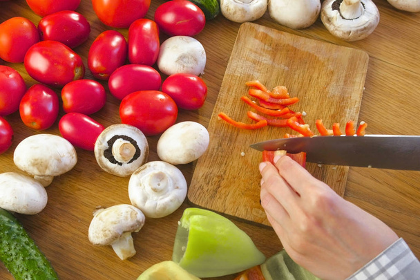 Womans kéz húzza zöldpaprikát fából készült táblán a konyhaasztalon, zöldségekkel. - Fotó, kép
