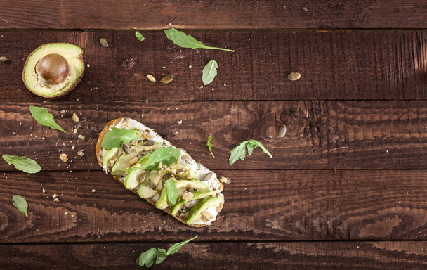 Closeup of bruschetta with avocado, mascarpone, rucola and nuts on a wooden table. - Foto, afbeelding
