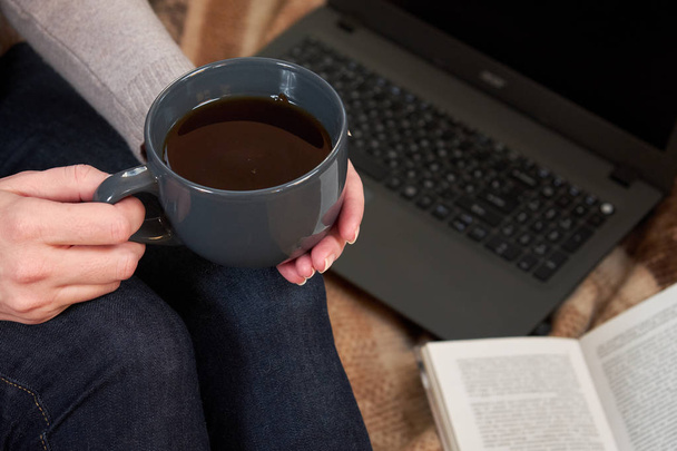Woman with a Cup of tea, a book,  mittens and a laptop on a blanket. Selective focus - Фото, зображення