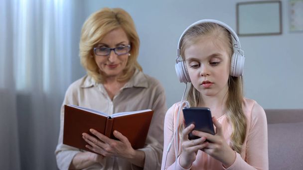 Mädchen mit Kopfhörern hört Musik und Oma liest Buch, Generationenlücke - Foto, Bild