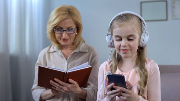 Little girl in headphones listening to book record elderly woman grandma reading - Foto, immagini