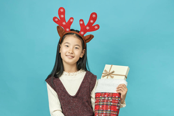 クリスマス コンセプトの頭飾りとアジアの女の子子は分離された青の背景にかわいいアジア女の子のクローズ アップ. - 写真・画像